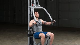Body Solid Powerline BSG10X review: A man sits on the machine's adjustable seat to perform a chest strengthening exercise