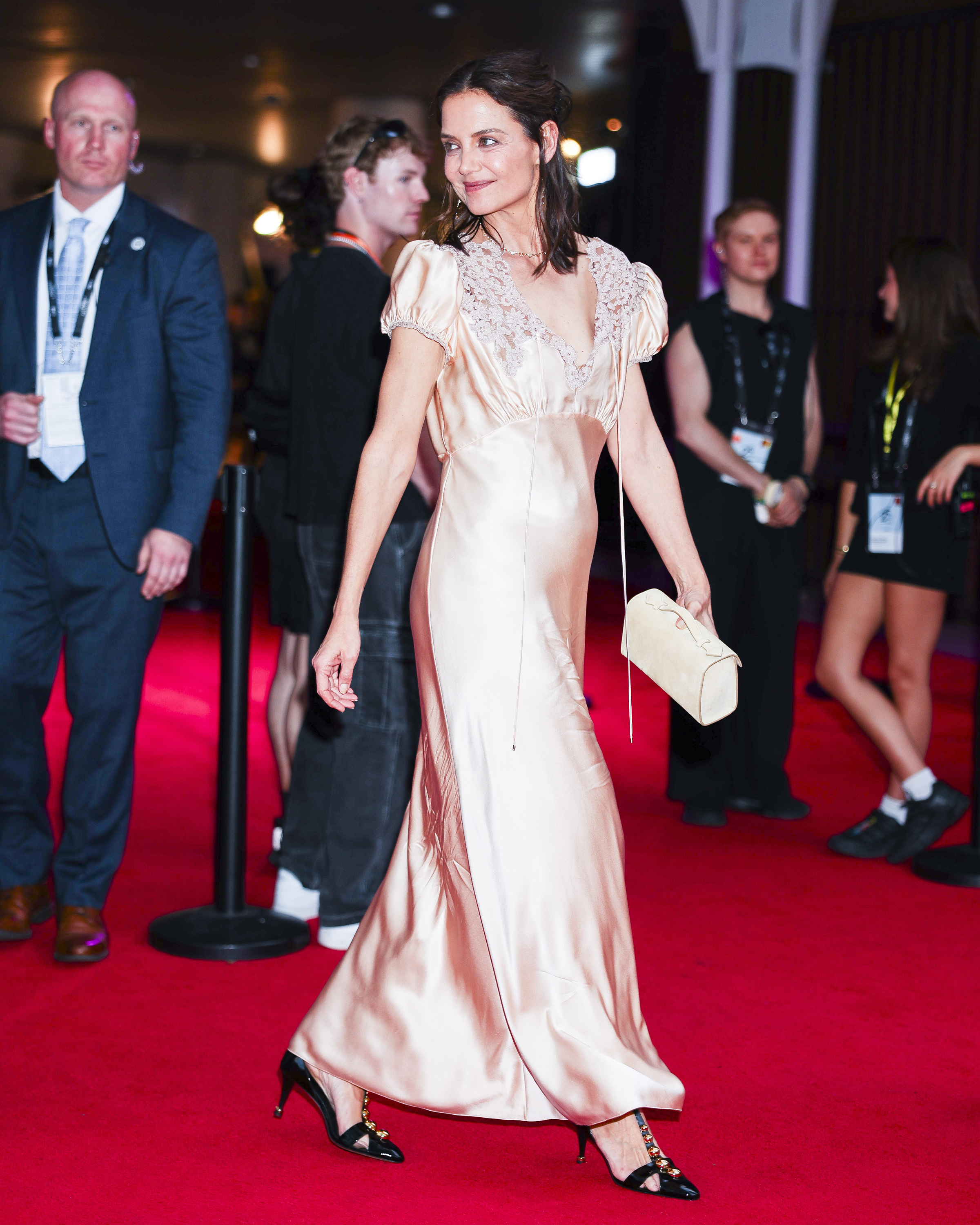 Katie Holmes walks a red carpet wearing a pink satin dress with t-bar heels.