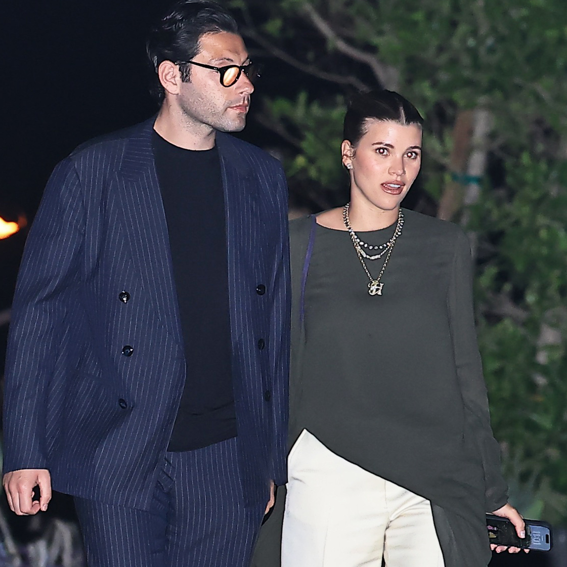 Sofia Richie and Elliot Grainge at Nobu Malibu, and she's wearing an asymmetrical long-sleeve gray top with wide-leg white pants and purple satin Dries Van Noten wedge mules