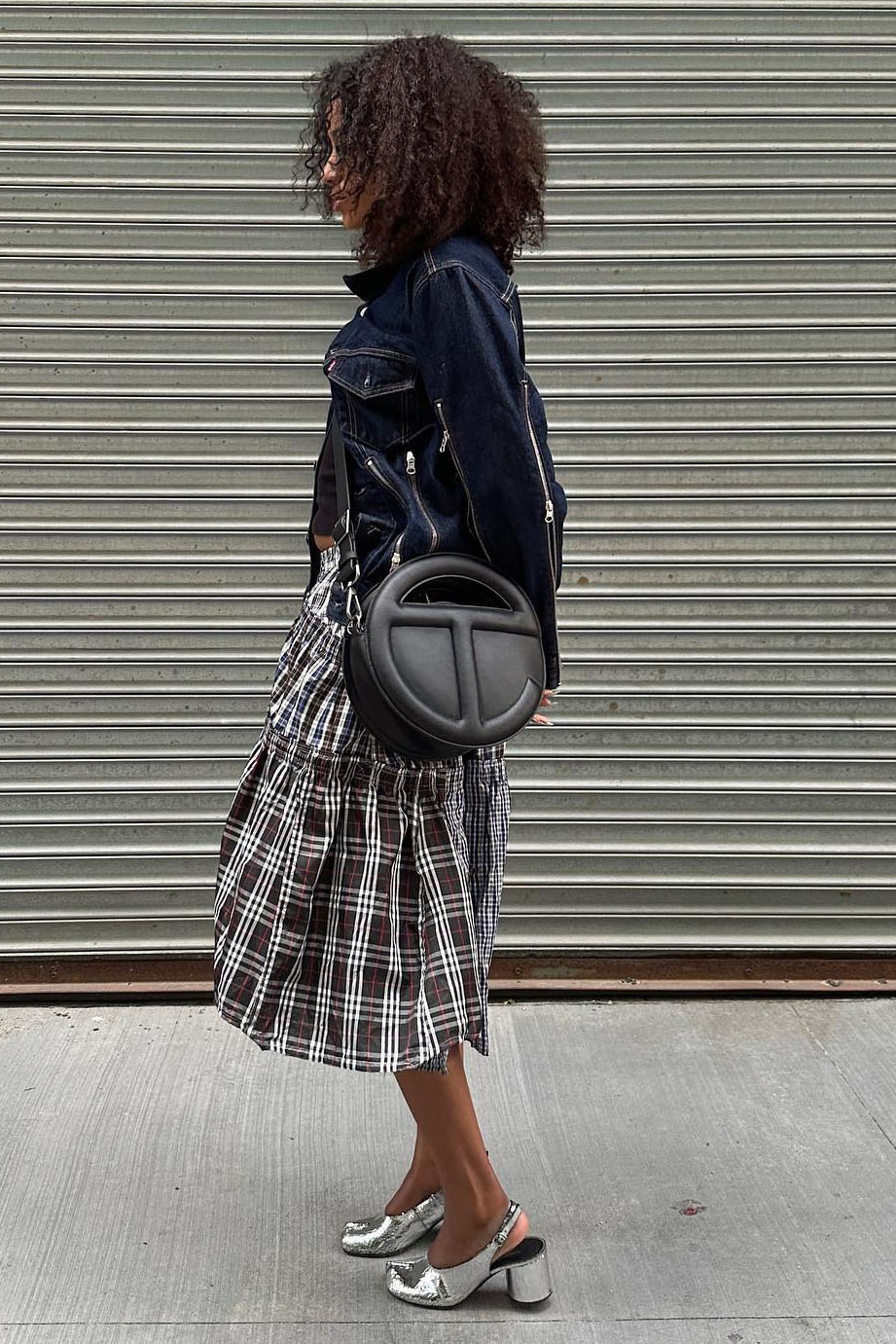 A woman wearing a denim jacket, plaid skirt, and silver heels
