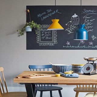 blue and yellow pendant lights hanging above a wooden dining table with a blackboard in the background