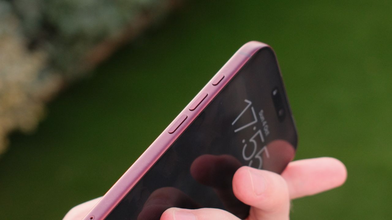 Close-up of the side buttons and front display of a burgundy iPhone 18 Pro Max held outdoors.