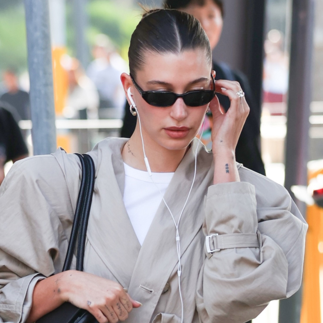 Hailey Bieber wearing a tan jacket, white pants, and kitten-heel pumps at the airport in Australia