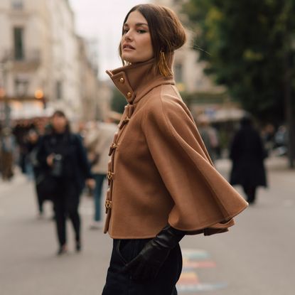 fashion week attendee wearing beige cape and leather gloves