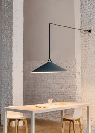 A large triangular light in blue, hanging from the wall through the specially designed rope, illuminating a dining table