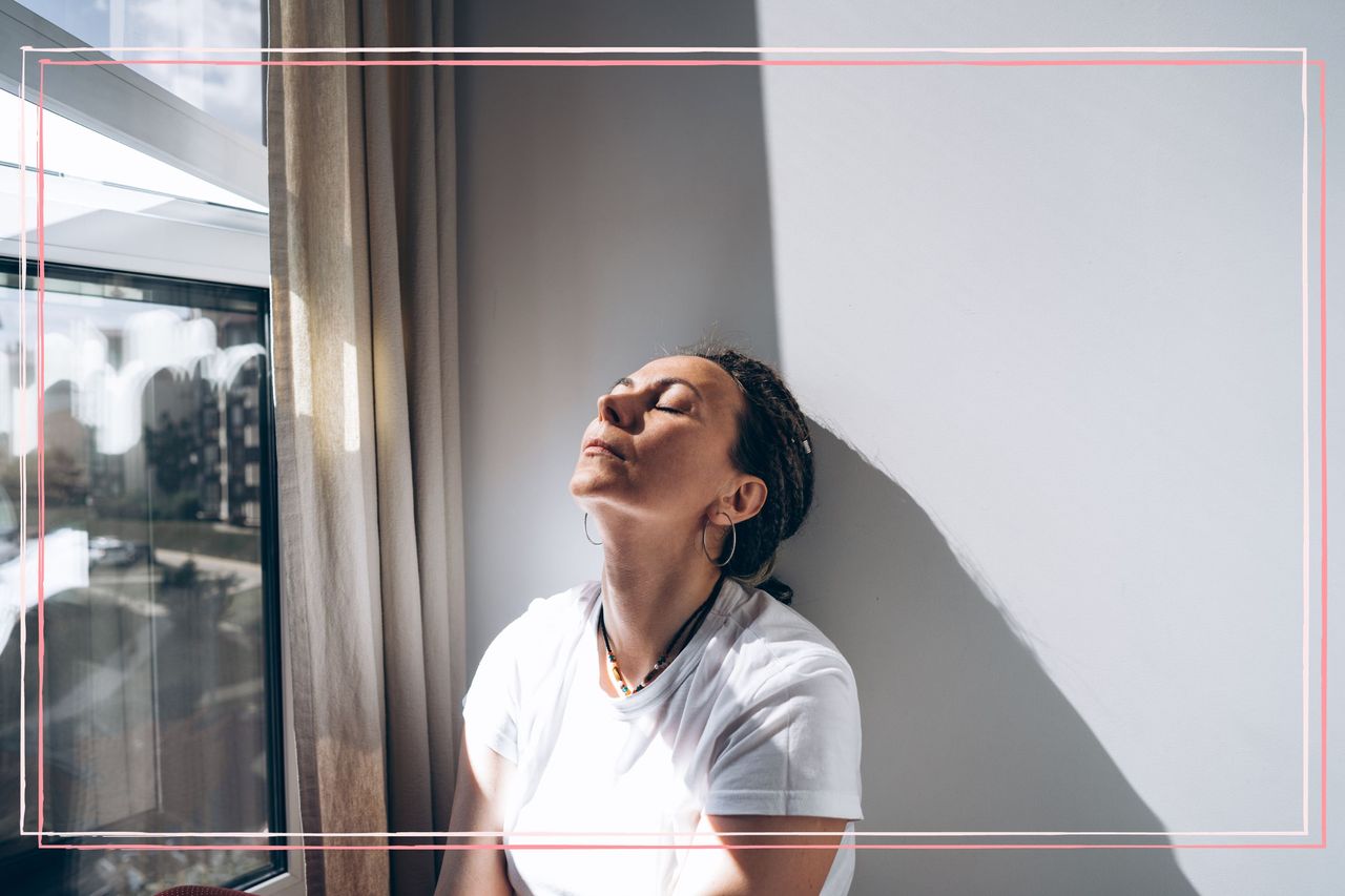 A woman sat by a window with her eyes closed and face turned upwards