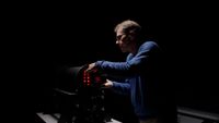 Man adjusting a camera or device with red lights in a dark room, illuminated by focused lighting