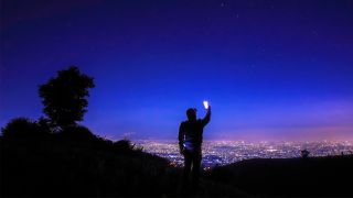 Smartphone astrophotography: How to take pictures of the night sky: image shows man holding smartphone against night sky