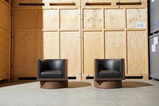 2 Black leather and wooden chairs on a concrete floor next to a large wooden crate