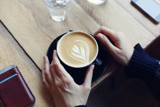 Overhead shot of hands holding a cup of coffee with latte art at a table.