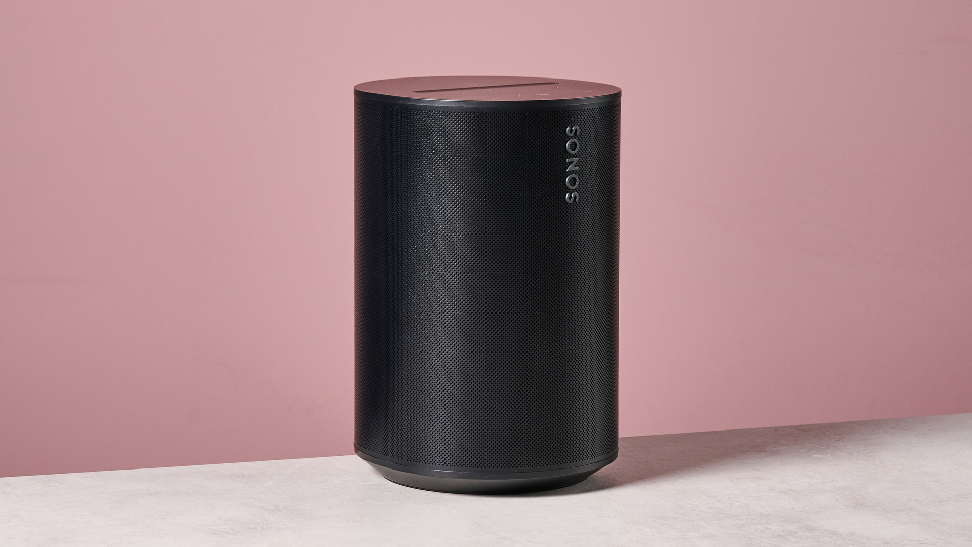 The Sonos Era 100 at a 45 degree angle in front of a pink background.