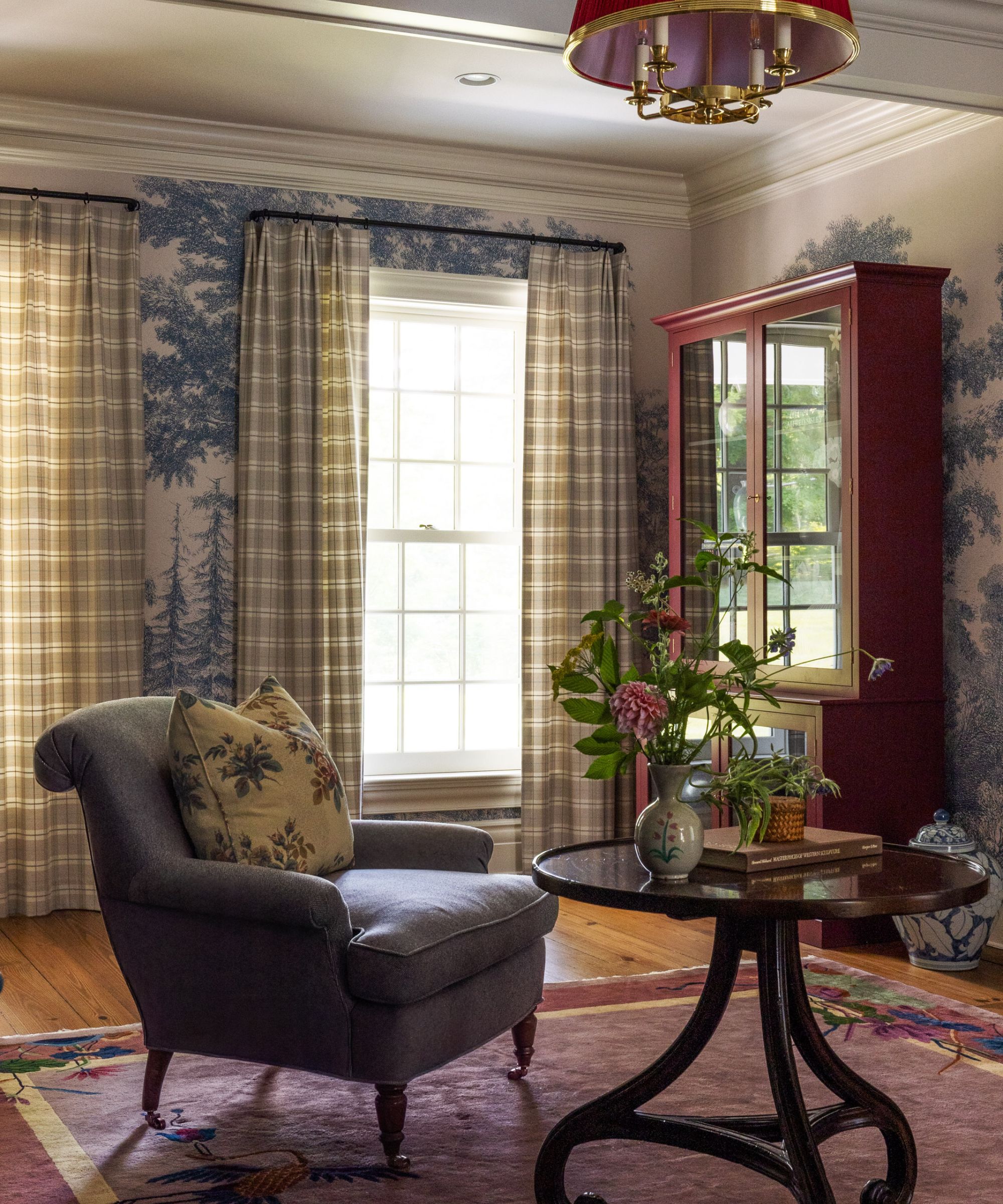 Traditional living room with blue and white wallpaper, armchair and round coffee table and red dresser