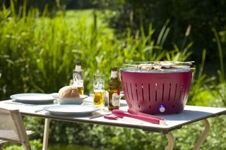 A Lotus Grill Smokeless BBQ from Cuckooland on an outdoor table with bbq tools and beers