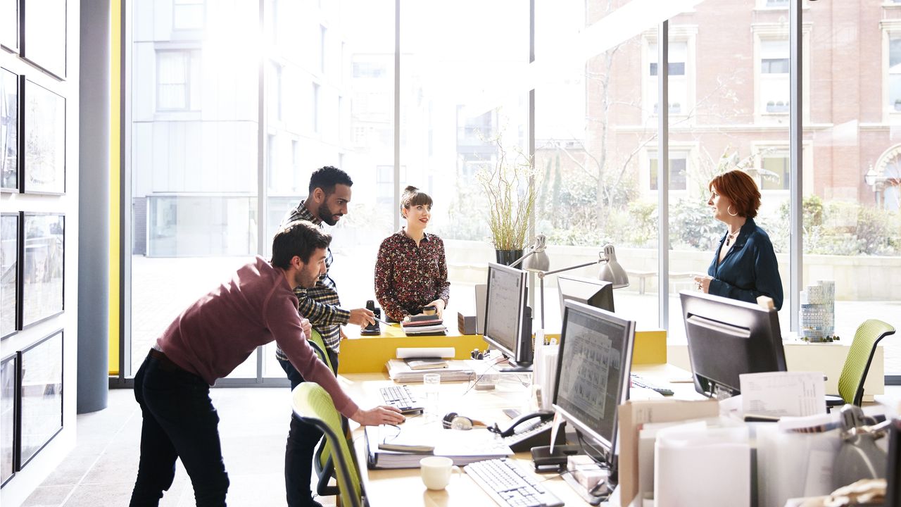 Four employees have a discussion around their desks.