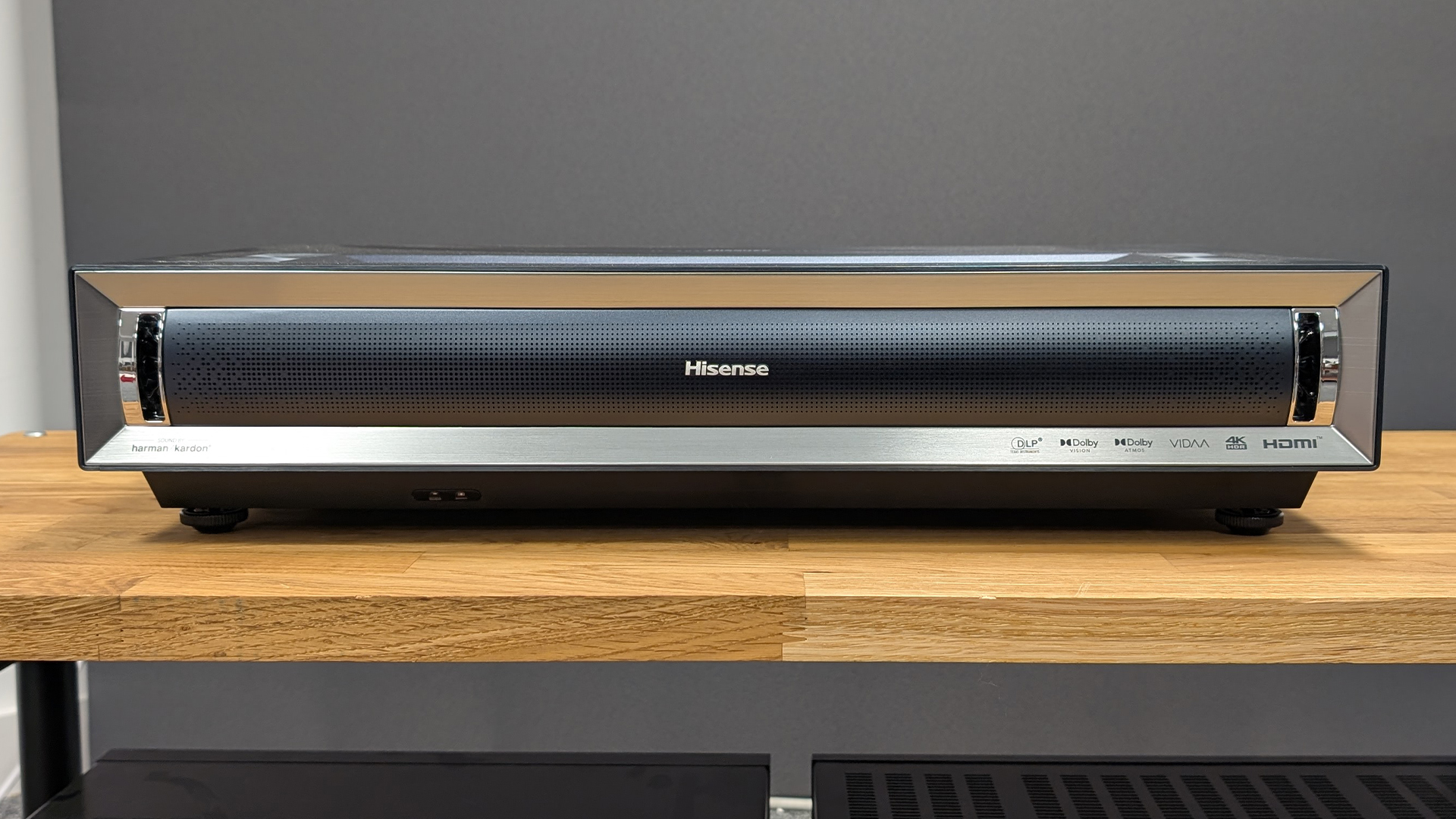 Hisense PX3 ultra short throw projector on wooden AV rack against grey wall
