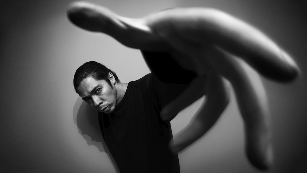 Fisheye lens character portrait of James Artaius, holding a distorted hand towards the camera
