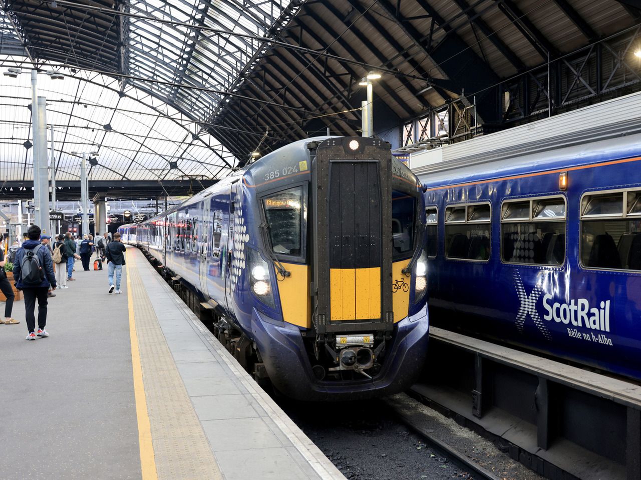 Two ScotRail trains at a train station with passengers walking past