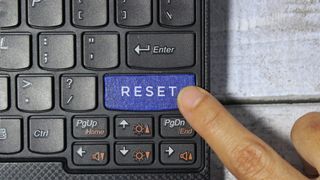 A finger pressing a button marked RESET on a keyboard.