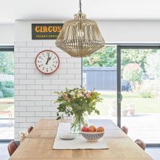 Orange clock on white tiled wall with white walls and a pendant light over a large wooden table