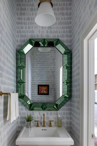 A small bathroom with a wallpaper behind the mirror