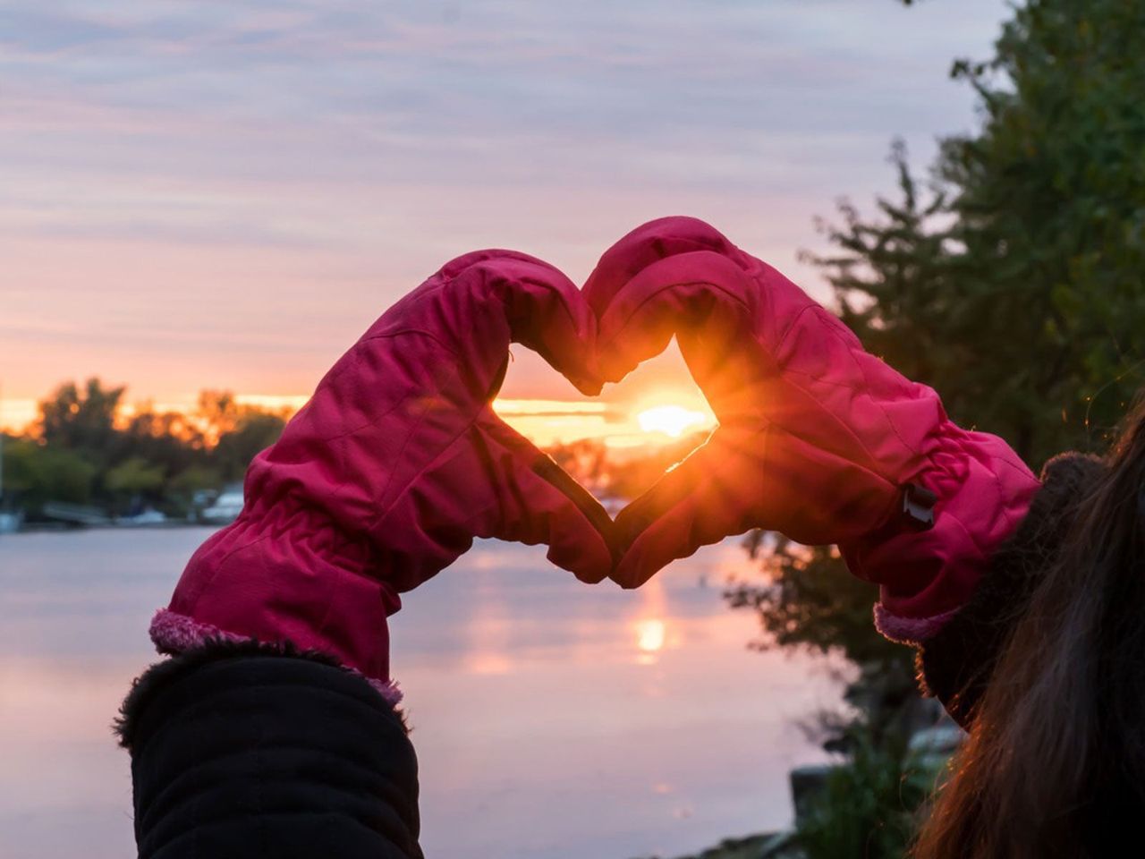 Hands With Gloves Making A Heart Shape Infront Of A Sunset