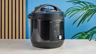 a black instant pot with a dial and touchpad is photographed against a blue background