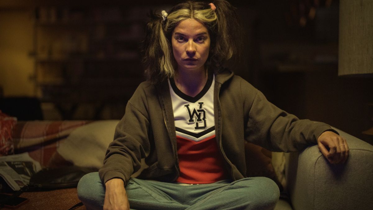 Annie Murphy sits on the couch in a daze, while wearing a cheerleader uniform in Black Mirror&#039;s. Joan Is Awful.