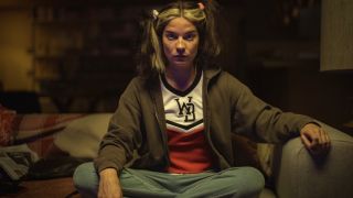 Annie Murphy sits on the couch in a daze, while wearing a cheerleader uniform in Black Mirror&#039;s. Joan Is Awful.