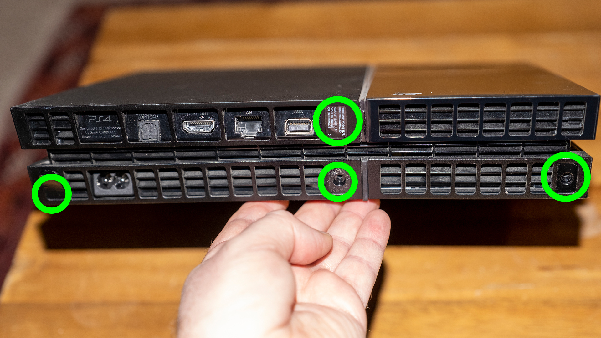 Фотография задней части PS4 с винтами, которые необходимо удалить, выделенными зелеными кружками.