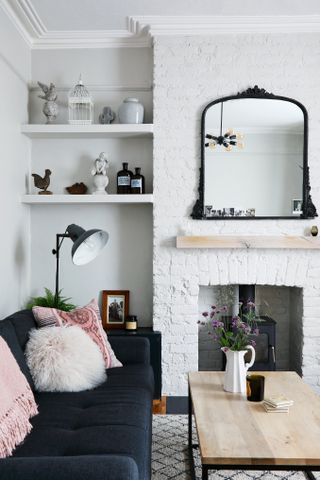 A white living room idea with black-framed mirror, white fireplace, black floor lamp, shelves and pink cushion