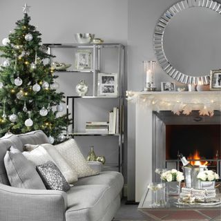 Silver chrome festive living room, Christmas tree in small space behind sofa, lit fire.