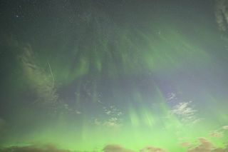 curtains of green lights appear to rain down from the starry sky, a long white streak of a meteor is visible in the middle left portion of the image.