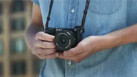 A man holding the Sony Alpha a6100, number 1 in our list of the best mirrorless cameras