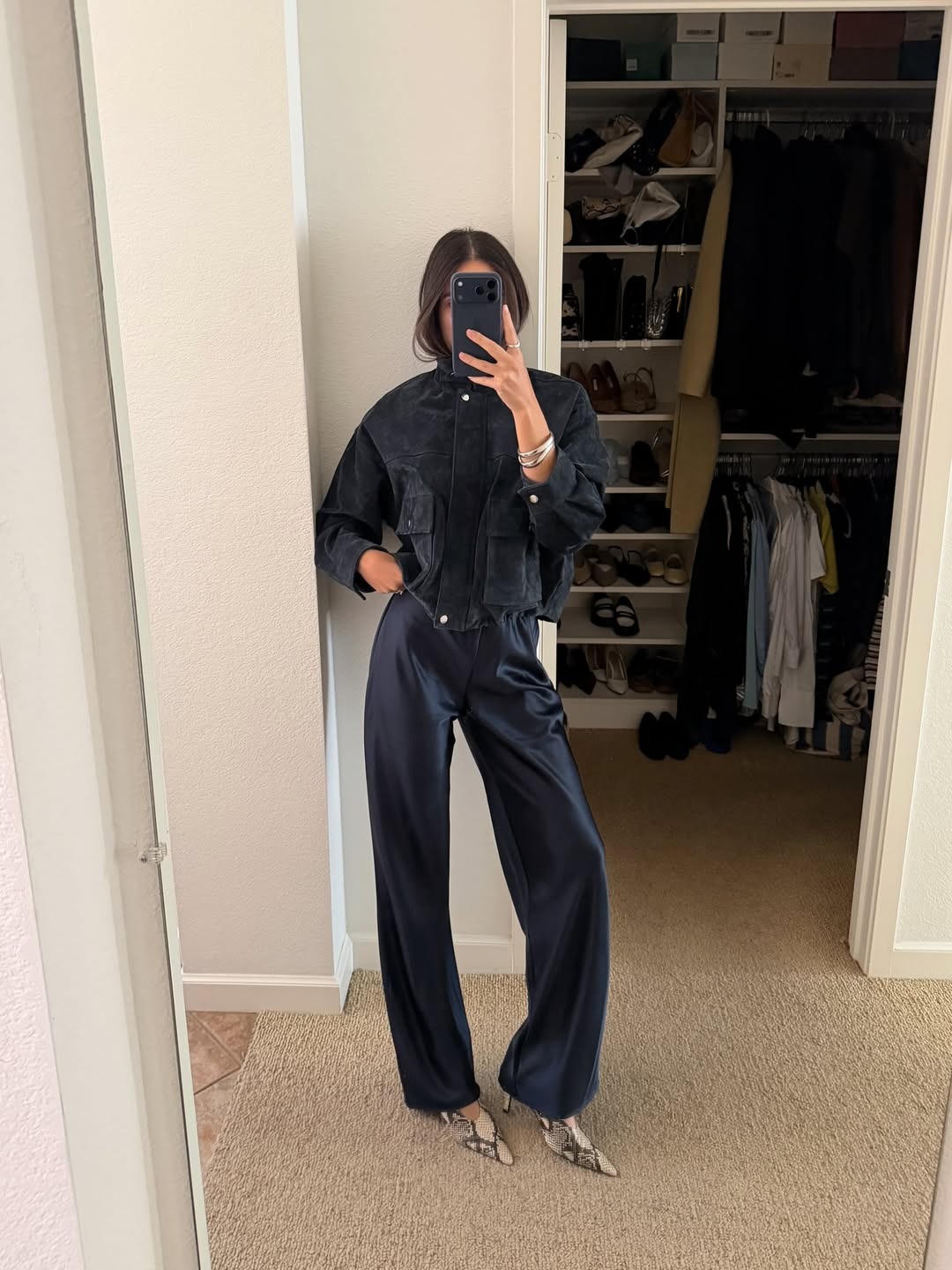 Ivana wears the Reformation Gale Satin trousers in navy, and a black bomber jacket, and snake print shoes