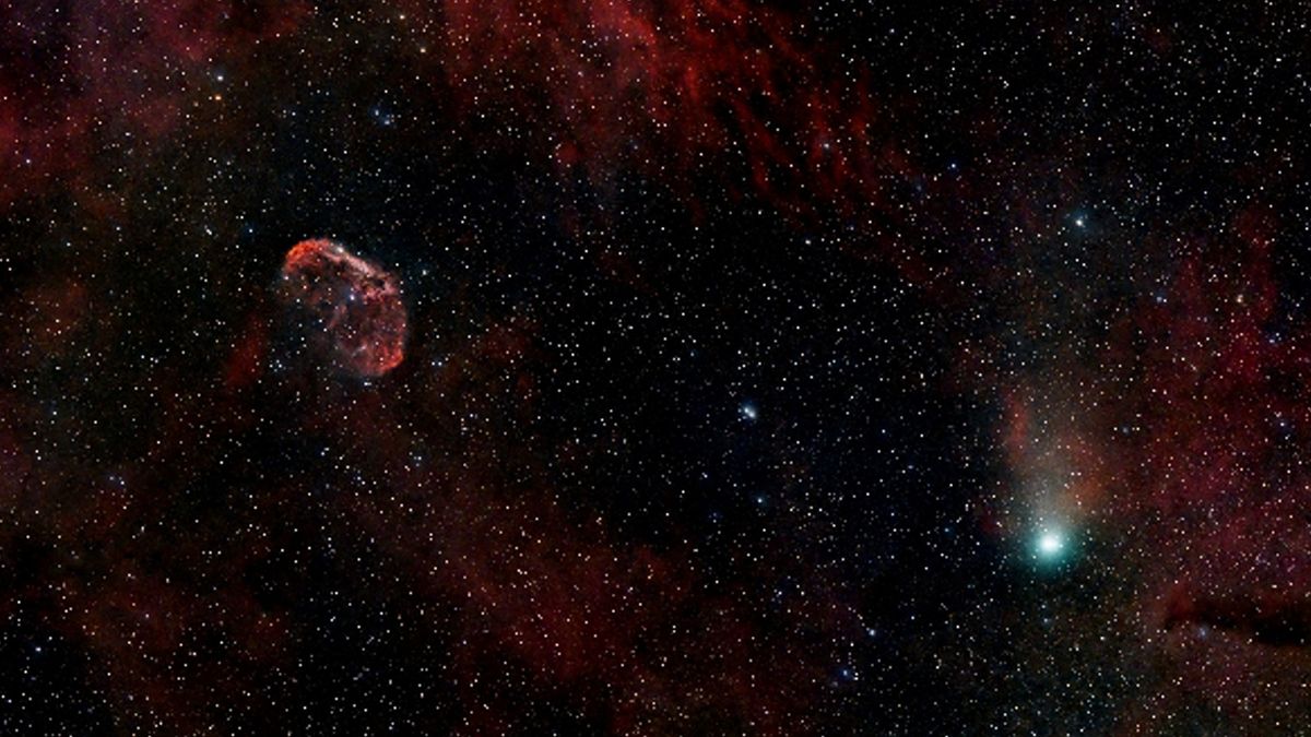 A green <b>comet</b> next to a red, crescent-shaped nebula. 