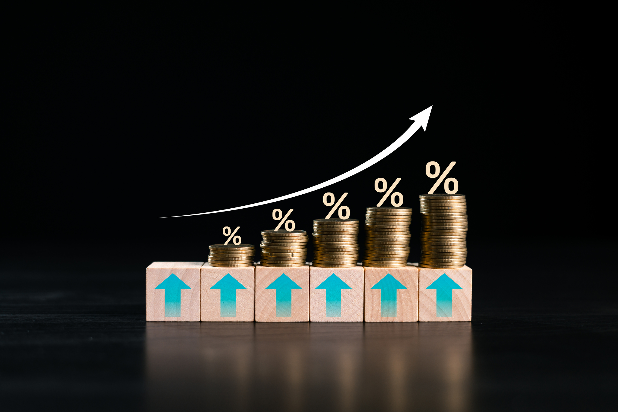 Rising coin stacks on wooden blocks with percent signs and growth arrow on black background