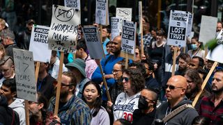 Amazon workers at a walkout rally at the company's headquarters in Seattle, Washington, carrying signs protesting return to office mandates put in place by the company. Decorative: the employees have been photographed with a telephoto lens and are stood at a three-quarters angle to the photographer.