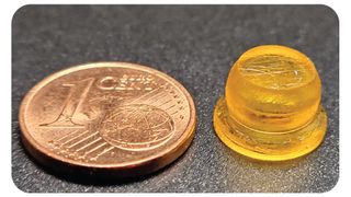 the yellow sucker-shaped device sitting on a table next to a one euro cent coin