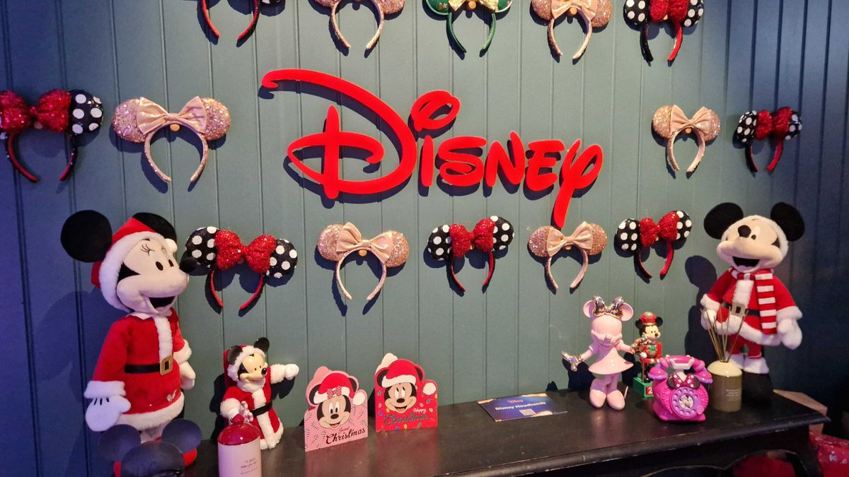 Disney logo surrounded by Minnie ears, toys, and merchandise against a wooden panelled wall