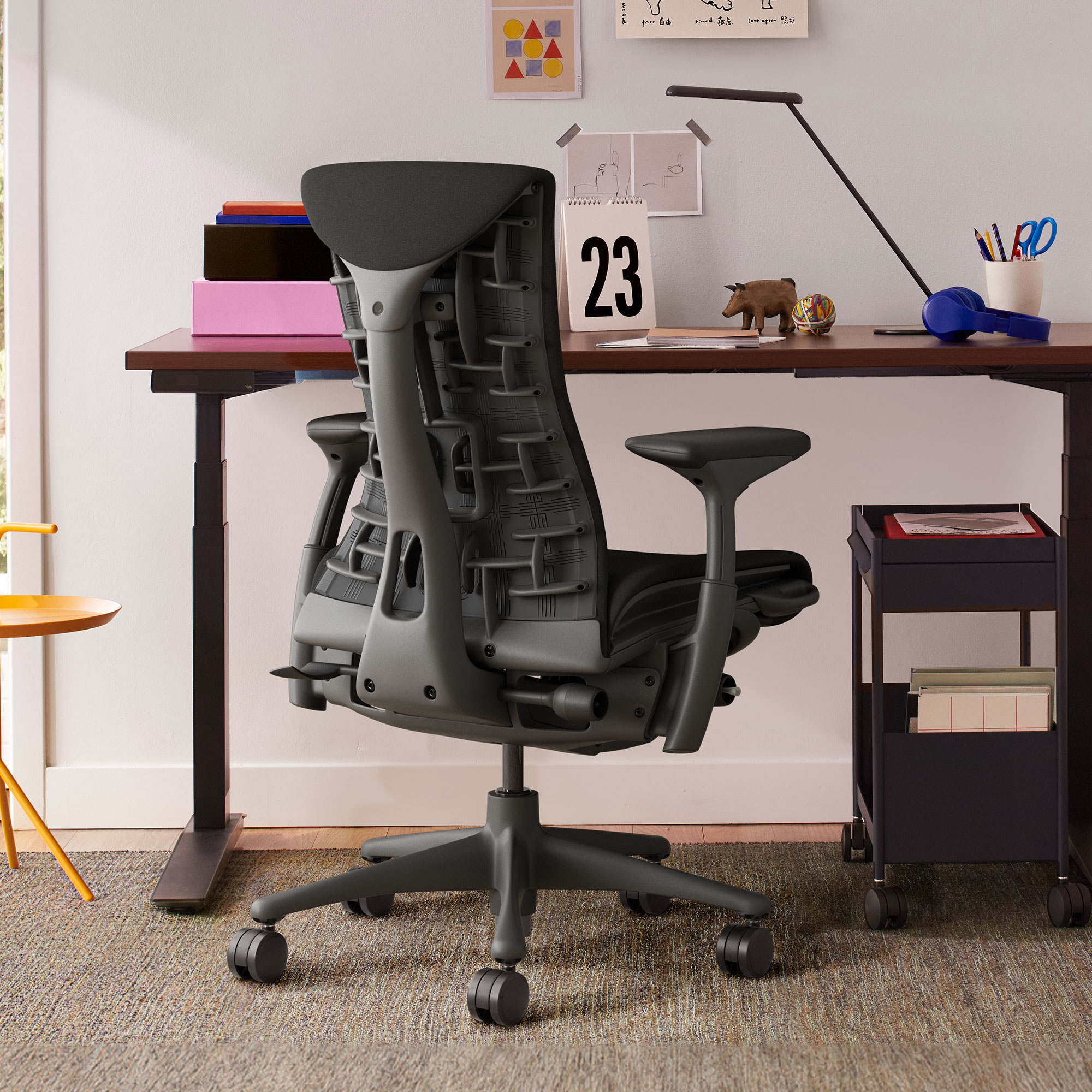 Black office chair on brown-grey rug at wooden desk with paper taped to wall in front