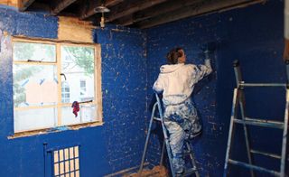 A woman on a ladder painting the brick walls bright blue