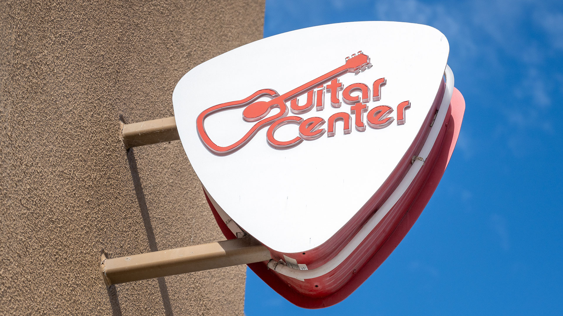 Close-up of pick-shaped logo sign at Guitar Center store in Emeryville, California with logo visible and blue sky behind