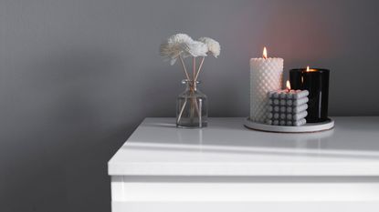 AI candles come in a range of styles: Three black, white, and grey candles on a side with a vase of dried flowers