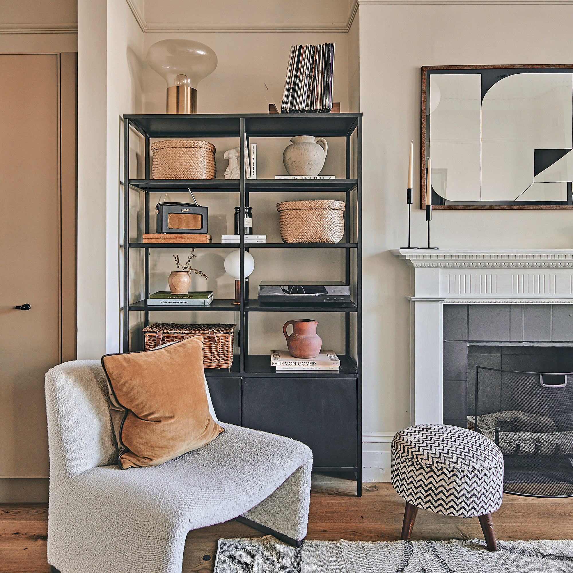 a living room with black metal alcove shelving a fireplace and traditional fire surround a boucle occasional chair and a zig zag patterned black and white footstool