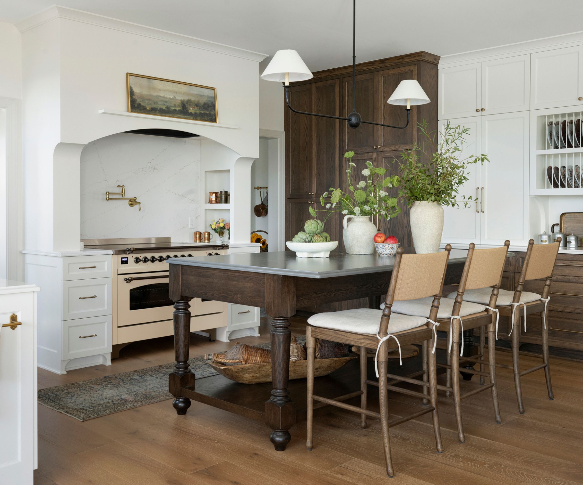 Kitchen with freestanding wooden island, wooden cabinetry, alcove with range oven and pot filler and vintage artwork