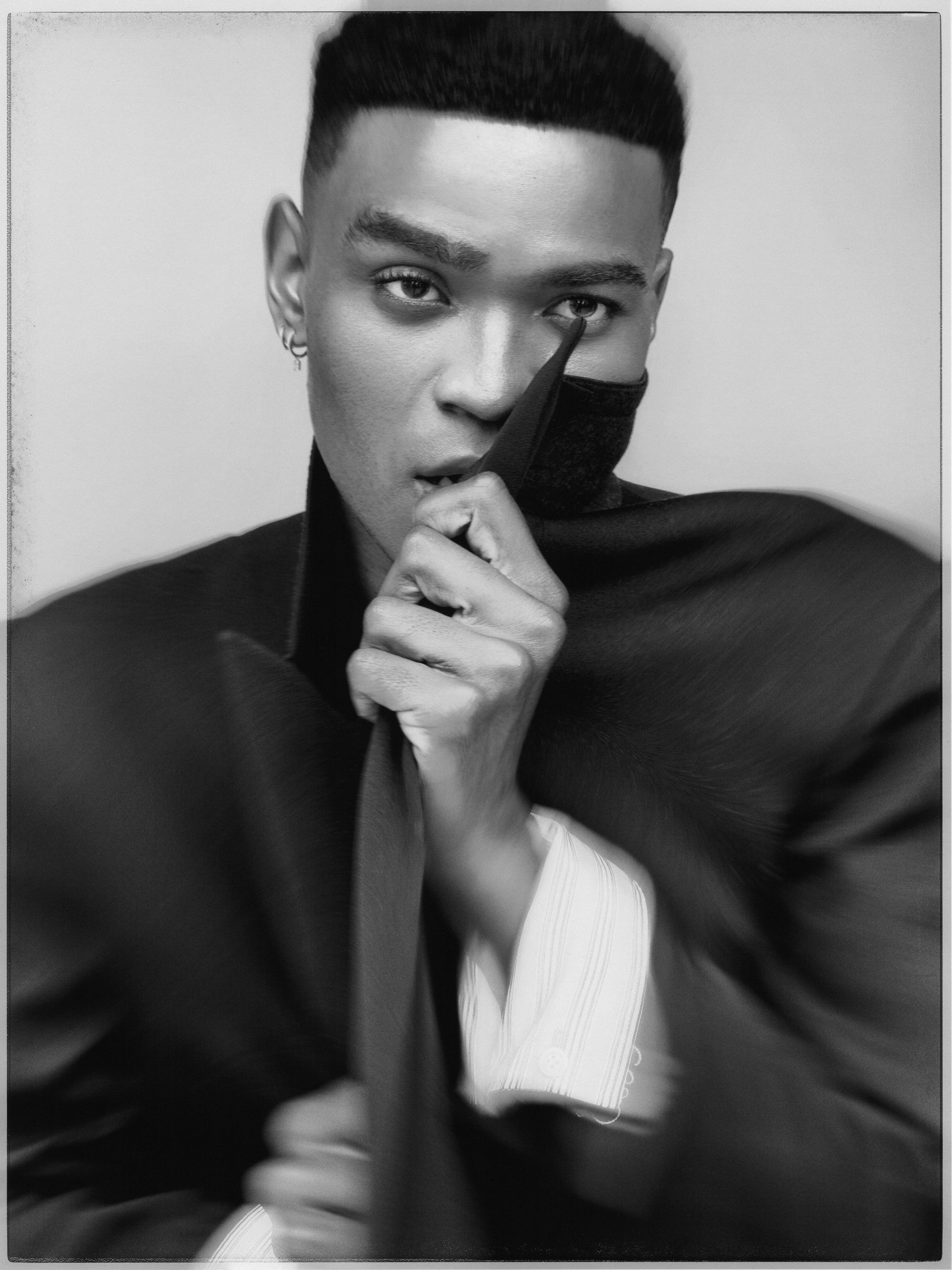 Owen Thiele poses in a black and white photo in which he pulls the collar of his black jacket with white cuffs