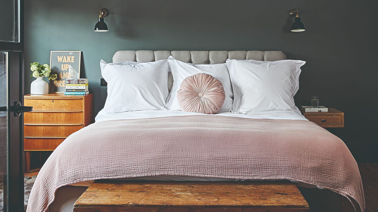 A dark small bedroom with a double bed with white bed linen and a blush pink throw