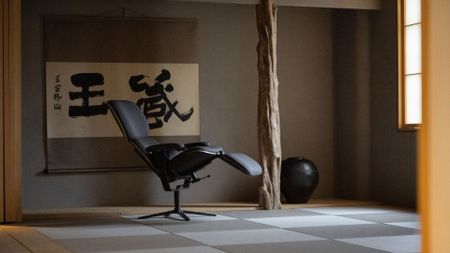 A gray wellness chair in a zen room with minimalist decor including a black vase and a wall hanging