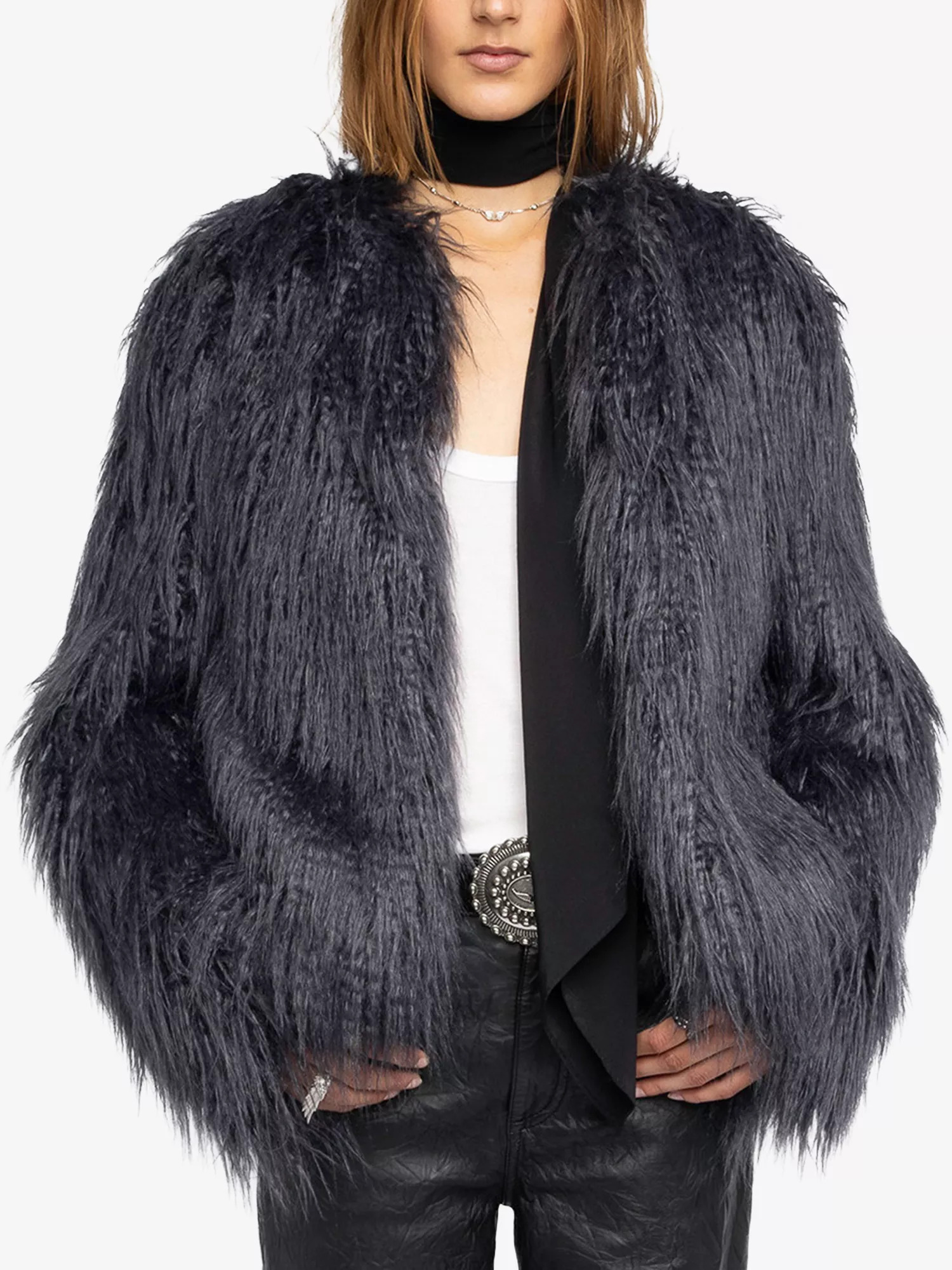 An image of a model wearing a grey, shaggy faux fur jacket with black leather pants, a black scarf and white vest.