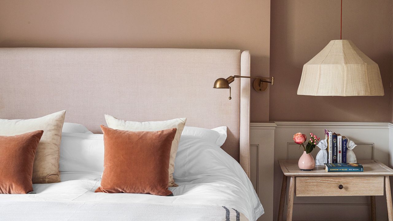 A bedroom with plaster pink walls and a bed with a cream headboard